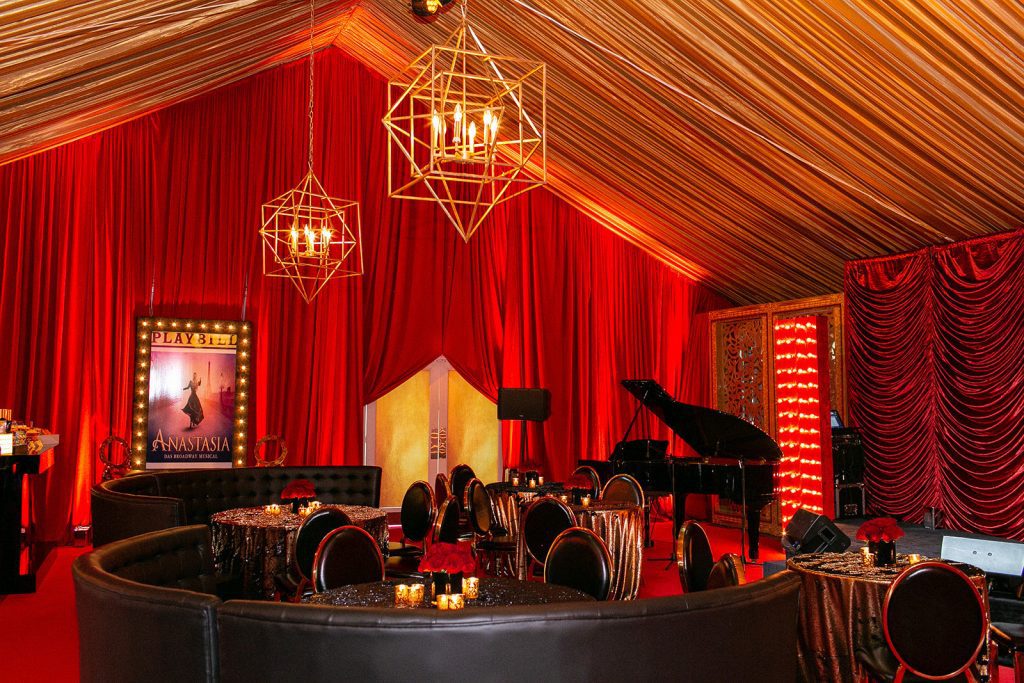 A red and black tent with a piano and chairs.